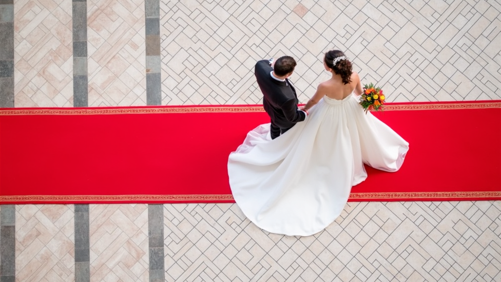 Dos recién casados caminan por encima de una alfombra roja. Plano cenital.